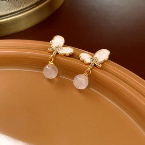 Detail of butterfly enamel earrings with pink stone drops and golden metallic frames