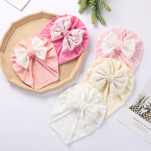 Detail of five infant turban hats in soft colors with delicate white lace bows on a tray