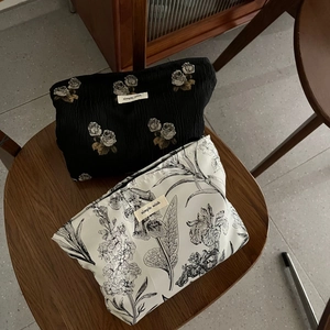 Floral jacquard makeup bags in black rose and botanical prints on a rustic stool