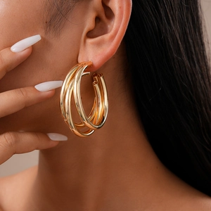 Close-up of golden multi-layer geometric C-shaped hoop earrings on a female model