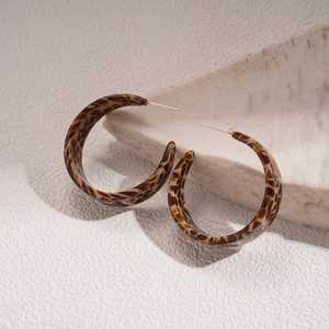 Detail of tortoiseshell acetate C-shaped hoop earrings on textured stone surface