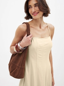 Detail of cream strap maxi dress featuring textured stitching and brown suede bag