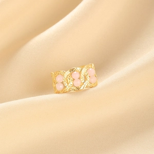 Detail of wide gold textured ring with six pink round gemstones on beige fabric