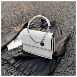 Close-up of white leather handbag with silver chain detail on a black leather jacket