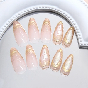French almond press-on nails with nude pink gradient, gold foil, and glitter accents
