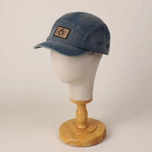 Vervaagde blauwe denim 5-panel pet met metalen ringpatch detail op een modelhoofd
