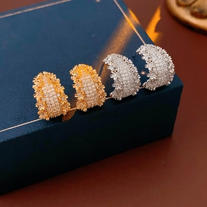 Détail de boucles d'oreilles en C dorées et argentées sur une boîte cadeau bleue