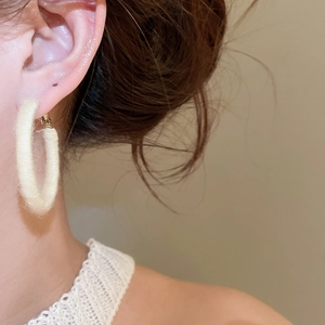 Close-up of cream-white knitted round hoop earrings showing detailed woven fabric texture