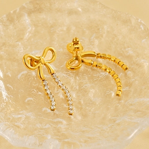 Golden bow tassel earrings with crystals on a textured glass plate in warm soft light