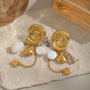 Detail von goldenen Schnecken-Ohrringen mit weißer Perle und Herzanhänger auf Papier