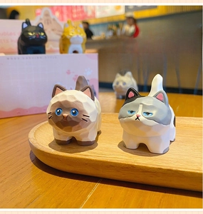 Close-up of geometric faceted resin cat figurines with pink themed gift packaging