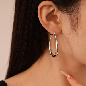 Close-up of a large polished silver teardrop hoop earring on a model with minimalist design