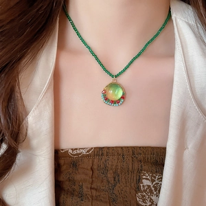 Close-up of a green beaded necklace with a vintage geometric resin pendant on a model