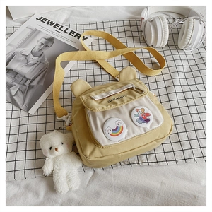 Detail of yellow canvas crossbody bag with cute badges and white plush bear charm accessory
