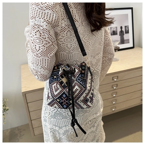 Detail of colorful geometric woven bucket bag with black leather strap on white lace dress