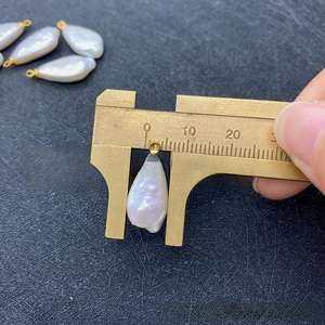 Macro view measuring the 10mm width of a baroque freshwater pearl drop with gold bail
