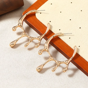 Macro shot of gold liquid lava metal drop earrings on minimalist jewelry display stand