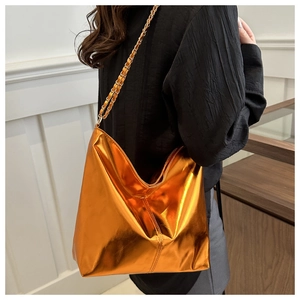 Side view of woman carrying orange metallic soft leather bucket bag with chain strap