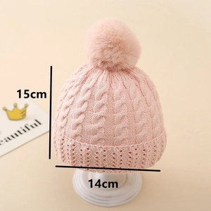 Detail view of pink baby knit hat with cable pattern and large pom pom showing dimensions