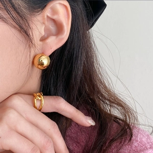 Detail showing high-polished golden spherical earrings and a twisted knot ring on a model