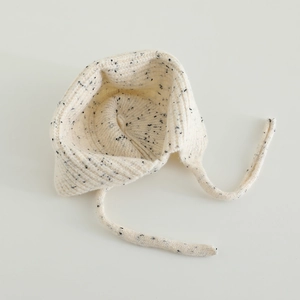 Gros plan d'un bonnet tricoté beige chiné pour bébé avec texture côtelée et longs liens