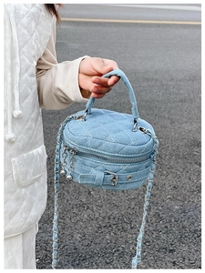 Close-up of blue denim quilted mini bag with metal buckle and chain strap being carried
