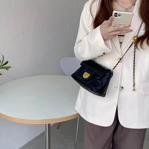 Model wearing a black quilted crossbody bag with gold chain strap in a cafe setting