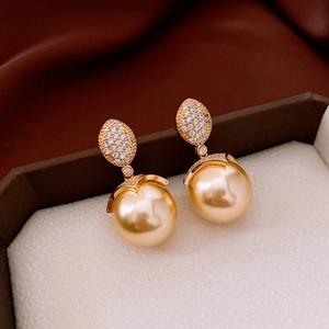 Macro shot of 18k gold plated pearl earrings with zircon encrusted leaf detail in a gift box