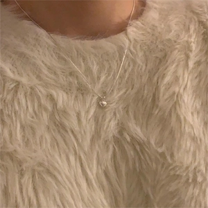 Close-up of minimalist silver heart necklace worn over a soft white plush sweater
