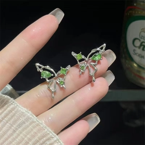 Detail of silver butterfly stud earring with sparkling green gemstones held by hand