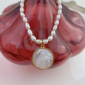 Macro detail of natural pearl necklace featuring a golden Virgin Mary shell pendant