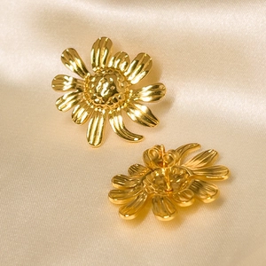 Detail view of 18K gold plated daisy flower earrings on champagne silk fabric background