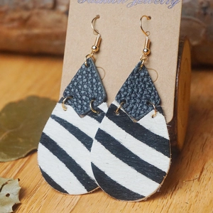 Vue détaillée des boucles d'oreilles en cuir motif vache noir et blanc avec crochets dorés