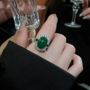 Gros plan d'une bague ovale style émeraude avec halo de zircons sur une main de femme