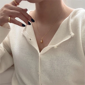Close-up of a minimalist gold teardrop pendant necklace paired with textured rings