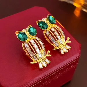 Macro view of gold owl earrings with green gem eyes and white crystal inlay on red box