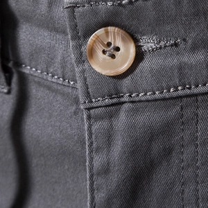Macro shot of charcoal grey trousers featuring a marble-textured button and neat stitching