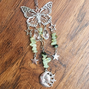 Detail of silver butterfly suncatcher with crystal pendants and green stones on wood