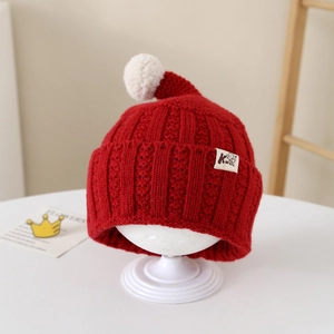 Close-up of red knit kids beanie featuring a white pompom and stitched letter K label