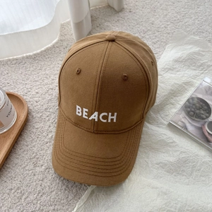 Detailed view of white BEACH embroidery on a brown cotton canvas baseball cap surface