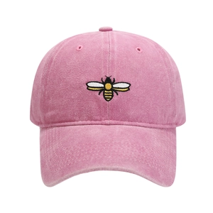 Close-up of a pink washed cotton baseball cap with detailed bee embroidery on the front