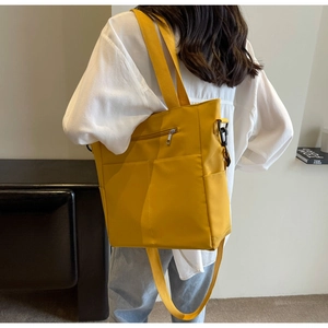 Model wearing a large yellow canvas tote bag with adjustable strap in bright indoor setting