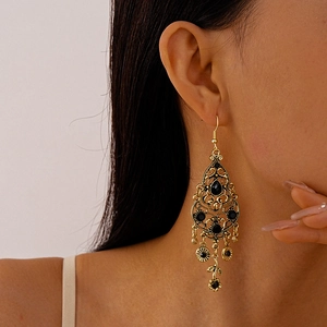 Macro detail of vintage gold hollow earrings with black gemstones worn by a model