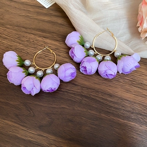 Detail of purple rose petals and white pearls on a golden metal hoop earring