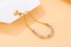 Detail of gold beaded chain bracelet featuring faceted grey beads and adjustable slider clasp