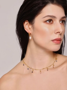 Detail of gold necklace with blue and pink stones and pearl earrings on a model