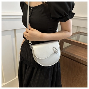 Close-up of a silver saddle bag with metallic finish and buckle on a black dress