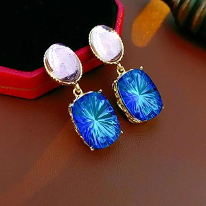 Detail of vintage gold earrings with pink oval stone and blue rectangular crystal drop