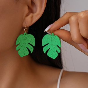 Detail of green monstera leaf earrings with wood texture on model for tropical vacation style