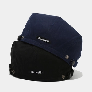 Detail of embroidered since 1991 patch and metal button on cotton twill beret hat